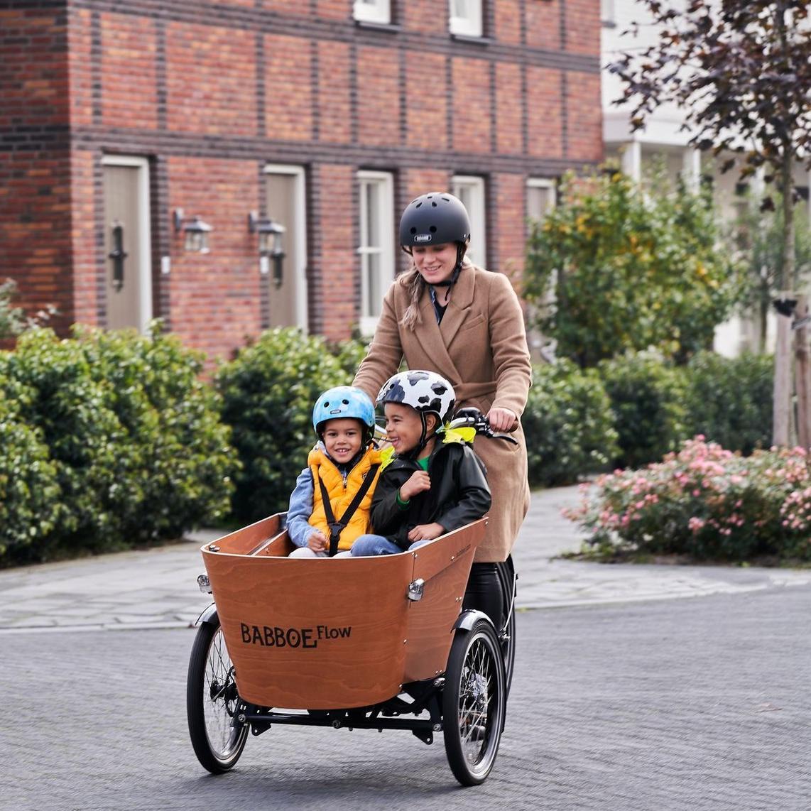 Eine Frau fährt mit dem Babboe Flow und zwei Kindern in der Transportbox über die Straße