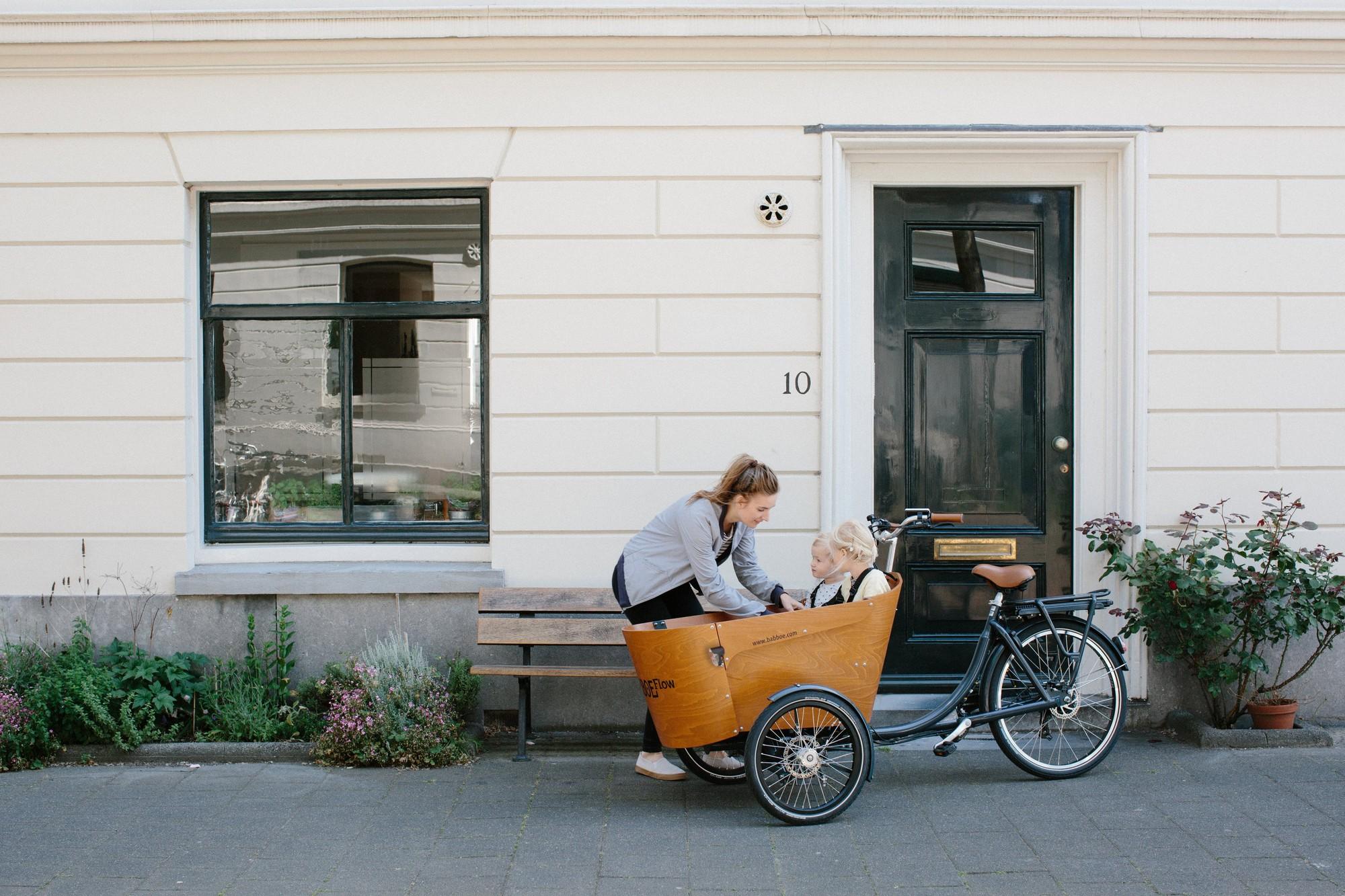 Eine junge Frau fährt ihre Kinder mit einem Babboe Lasten e-Bike in Karlsruhe zum Kindergarten.