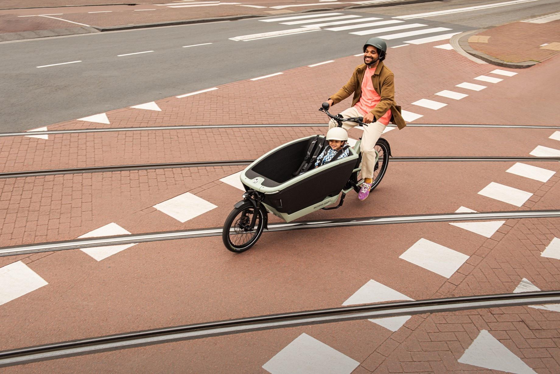Ein Mann fährt mit seinem Lastenrad von Urban Arrow und einem Kind in der Transportbox über die Straßenschienen