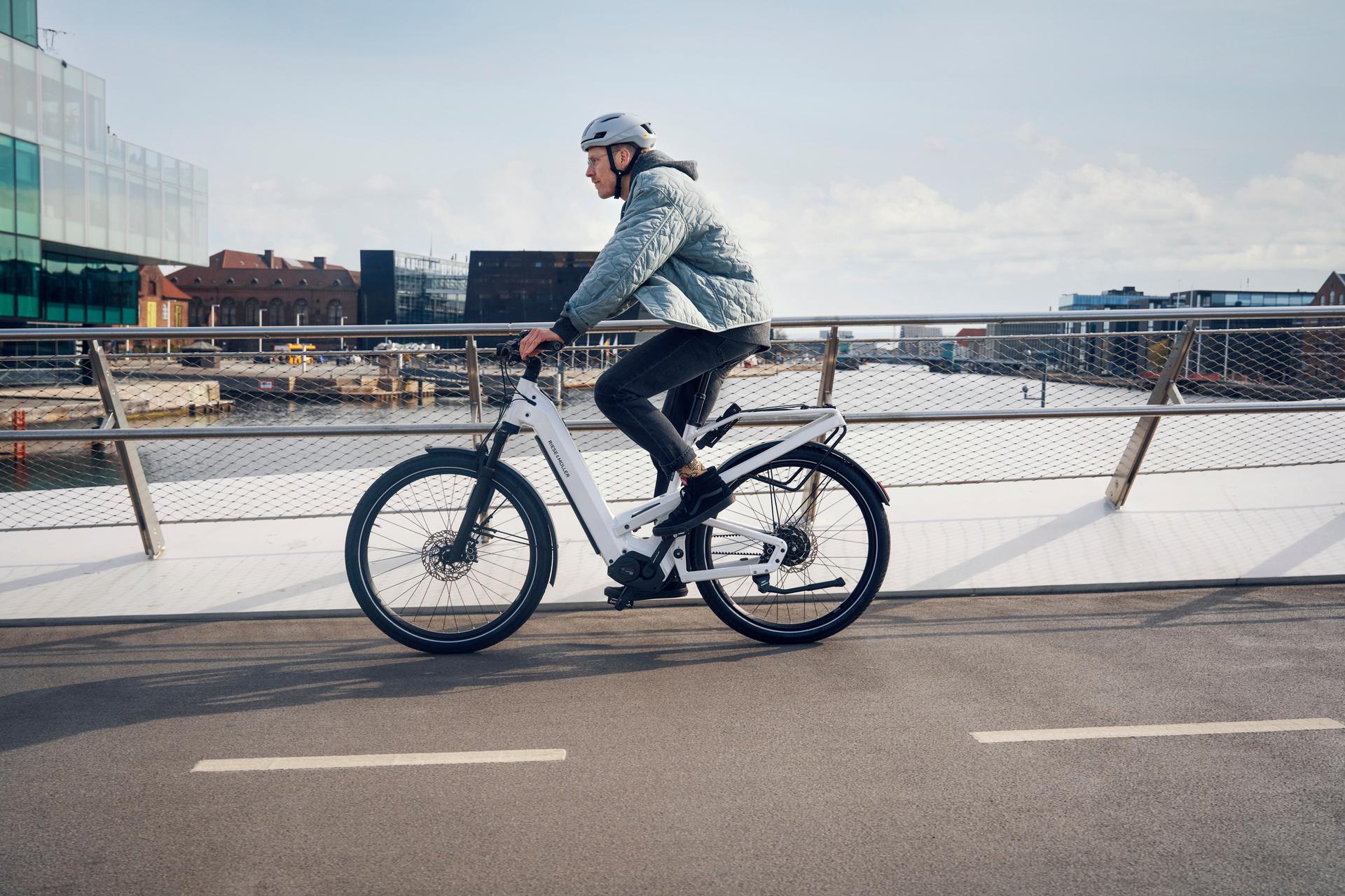 Person fährt mit einem weißen Riese & Müller Homage4 e-Bike über eine Brücke in urbaner Umgebung.