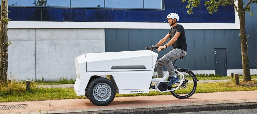 Mann fährt Urban Arrow Lastenrad auf Radweg in städtischer Umgebung