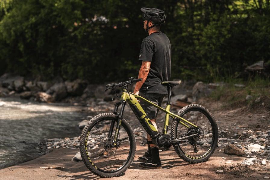 Mann mit E-Mountainbike am Flussufer im Grünen