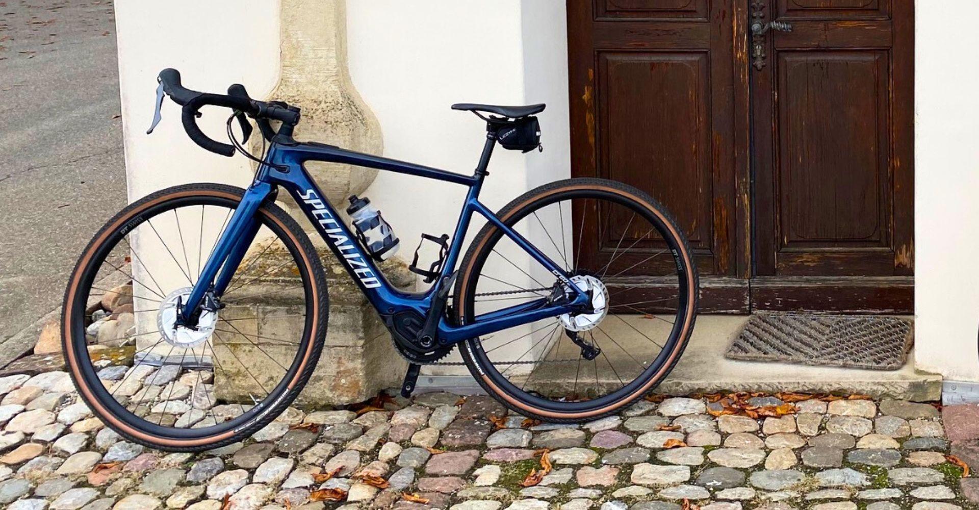 Das Bild zeigt ein Specialized Creo SL e-Bike, das an einer Wand mit Holztür abgestellt ist.