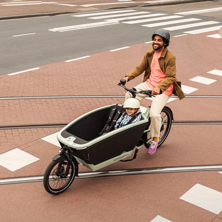 Ein Mann fährt mit seinem Lastenrad von Urban Arrow und einem Kind in der Transportbox über die Straßenschienen