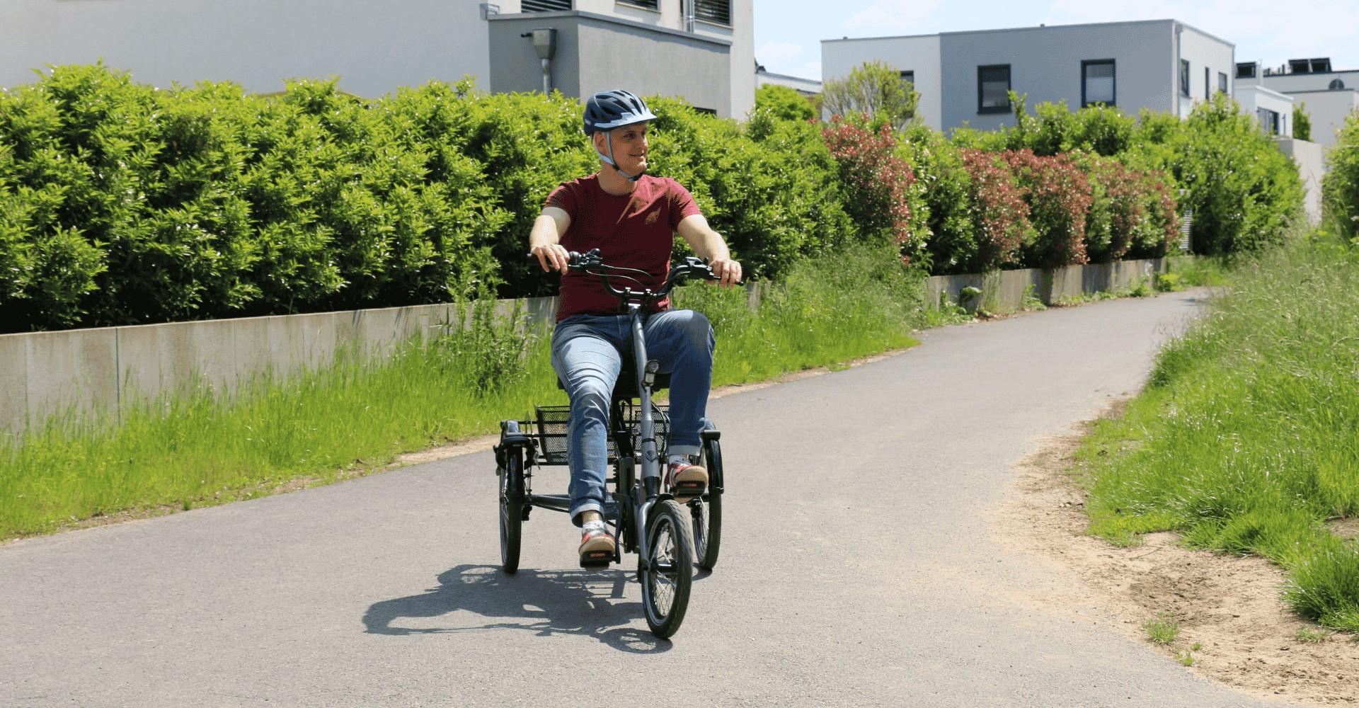 Ein Mann fährt mit dem Dreirad Scoobo eine Straße entlang im Grünen