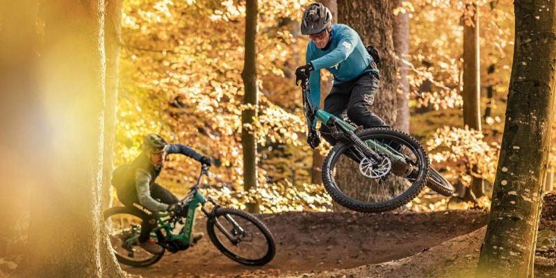 Zwei Mountainbiker im herbstlichen Wald bei Sprung und Abfahrt