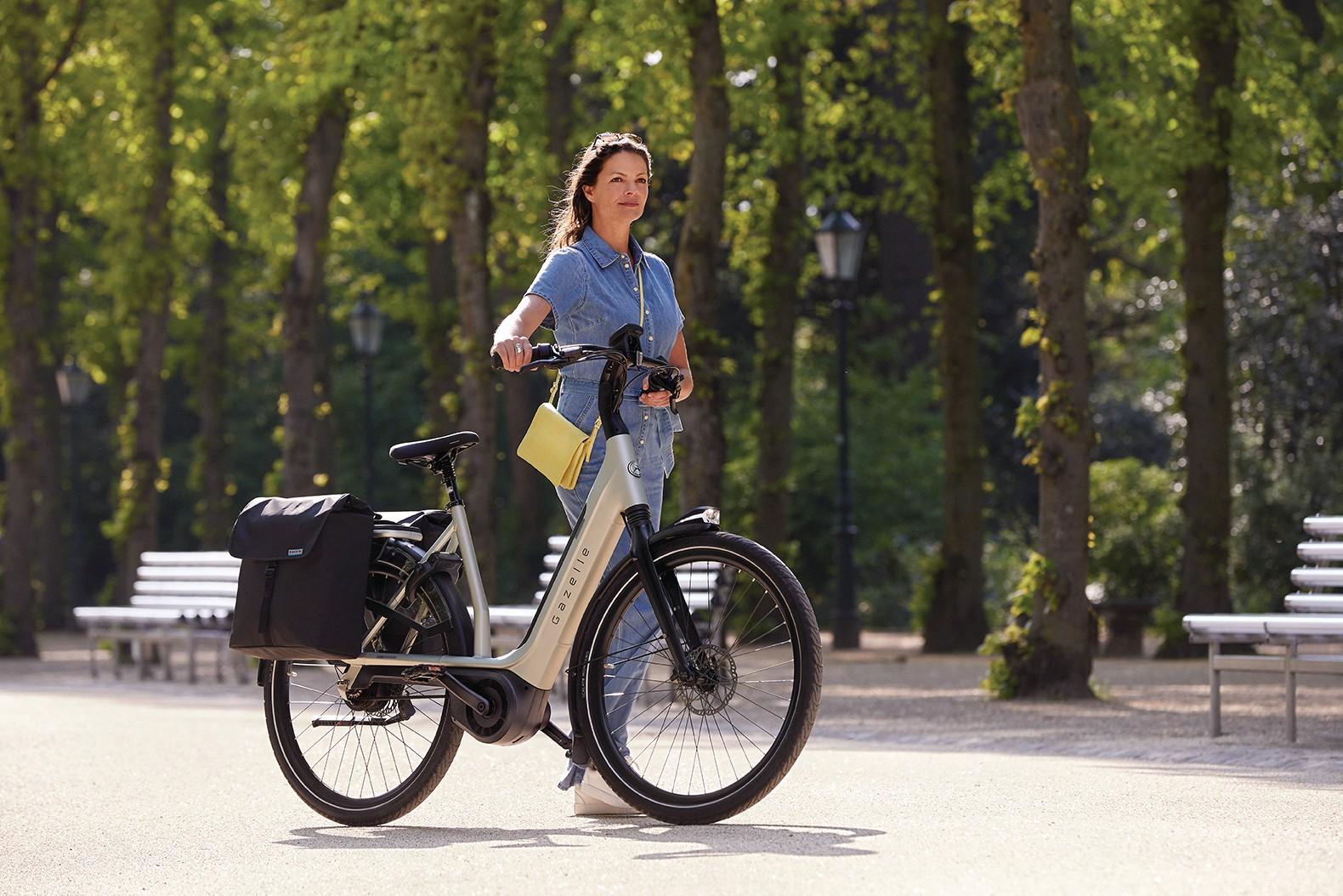 Eine Frau schiebt ihr Gazelle e-Bike mit Taschen durch den Park