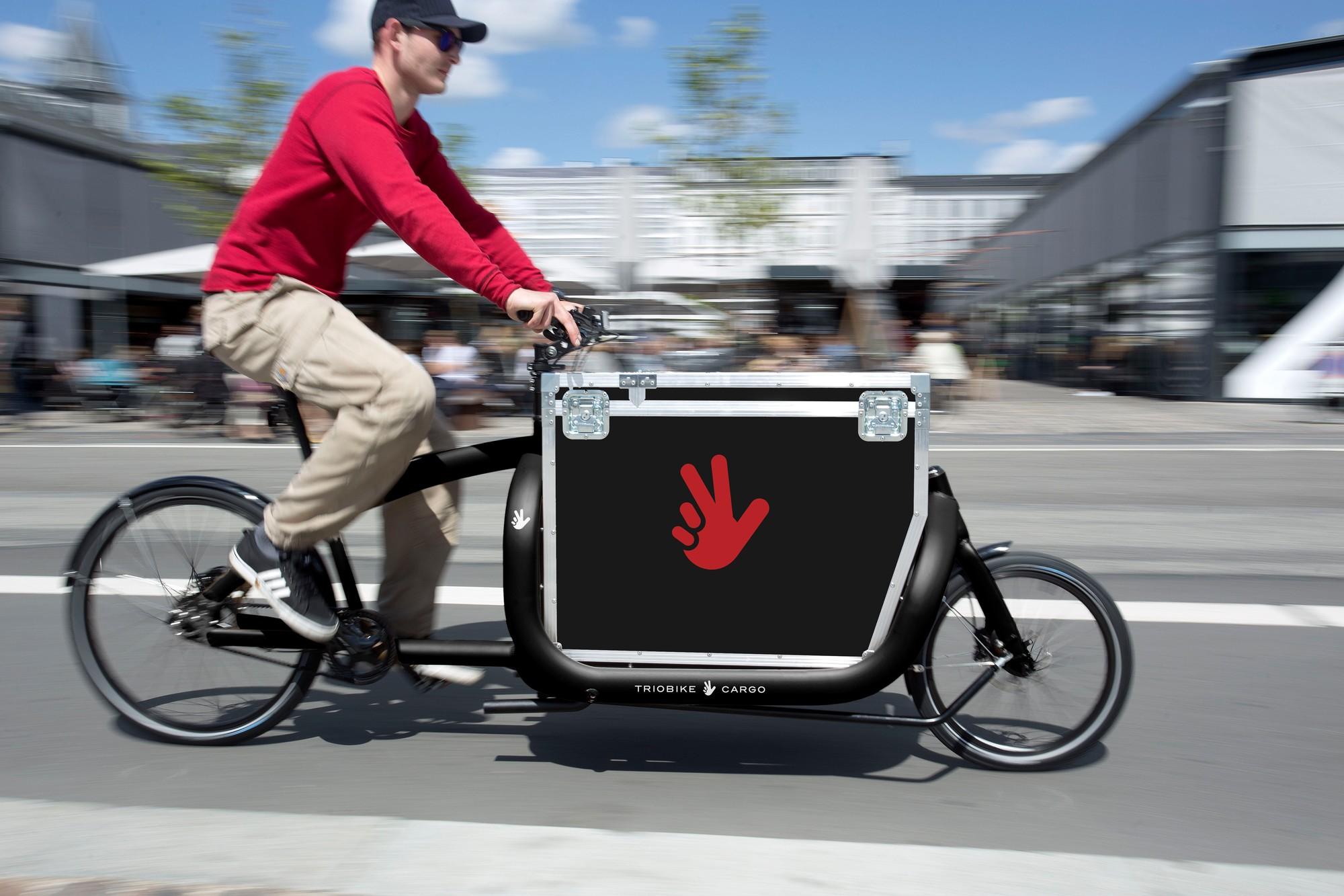 Ein Mann fährt auf dem Lastenrad Triobike Cargo schnell die Straße entlang