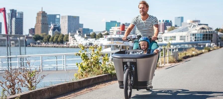 Mann fährt Carqon E-Lastenrad mit Kind auf städtischer Promenade
