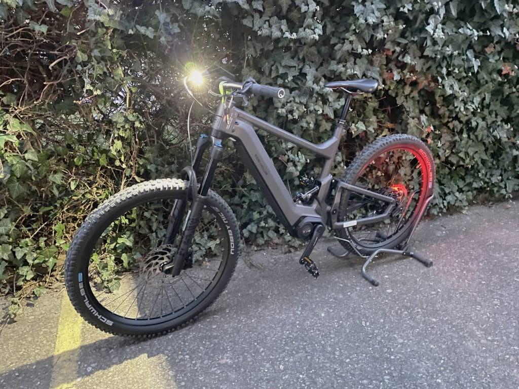 E-Bike mit eingeschaltetem Front- und Rücklicht auf Asphaltweg vor Hecke