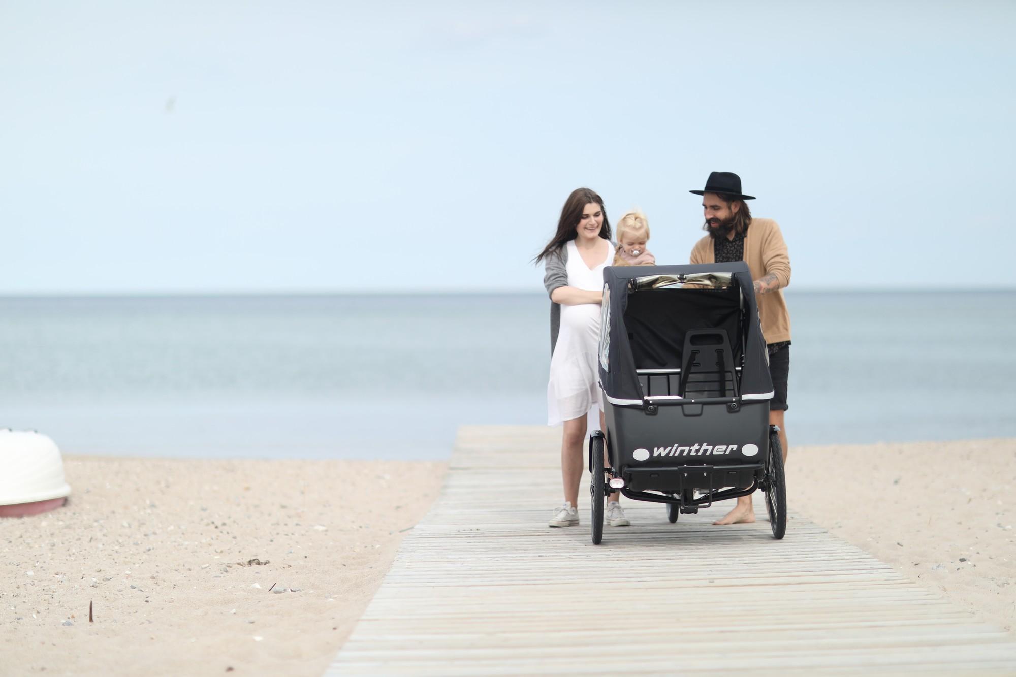 Eine Familie spaziert am Meer entlang mit dem Winther Kangaroo Lastenrad
