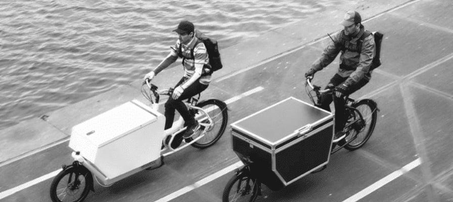 Zwei Lasten-e-Bikes mit großen Transportboxen am Flussufer