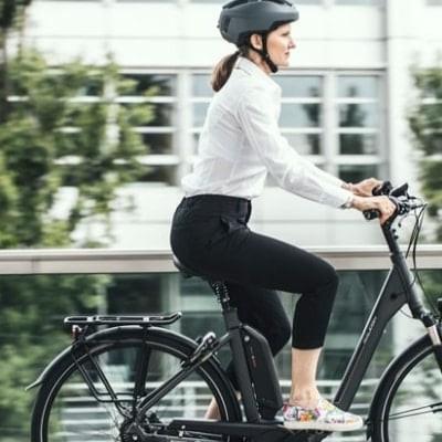 Frau auf E-Bike mit Helm vor Bürogebäude