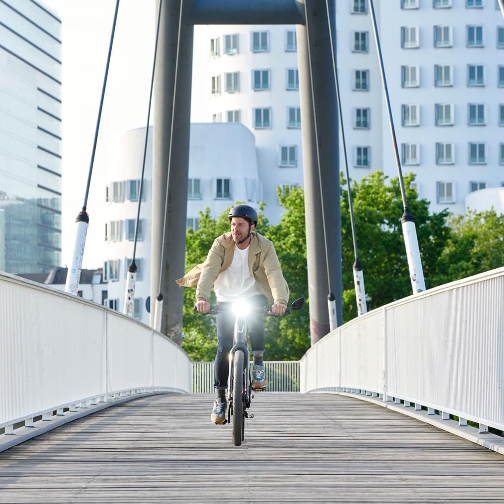 Ein Mann fährt mit einem E-Bike über eine Brücke in der Stadt. Perfekt für komfortable und umweltfreundliche Pendle