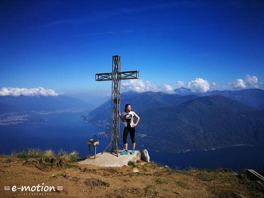 Person neben Gipfelkreuz mit Blick auf See und Berge