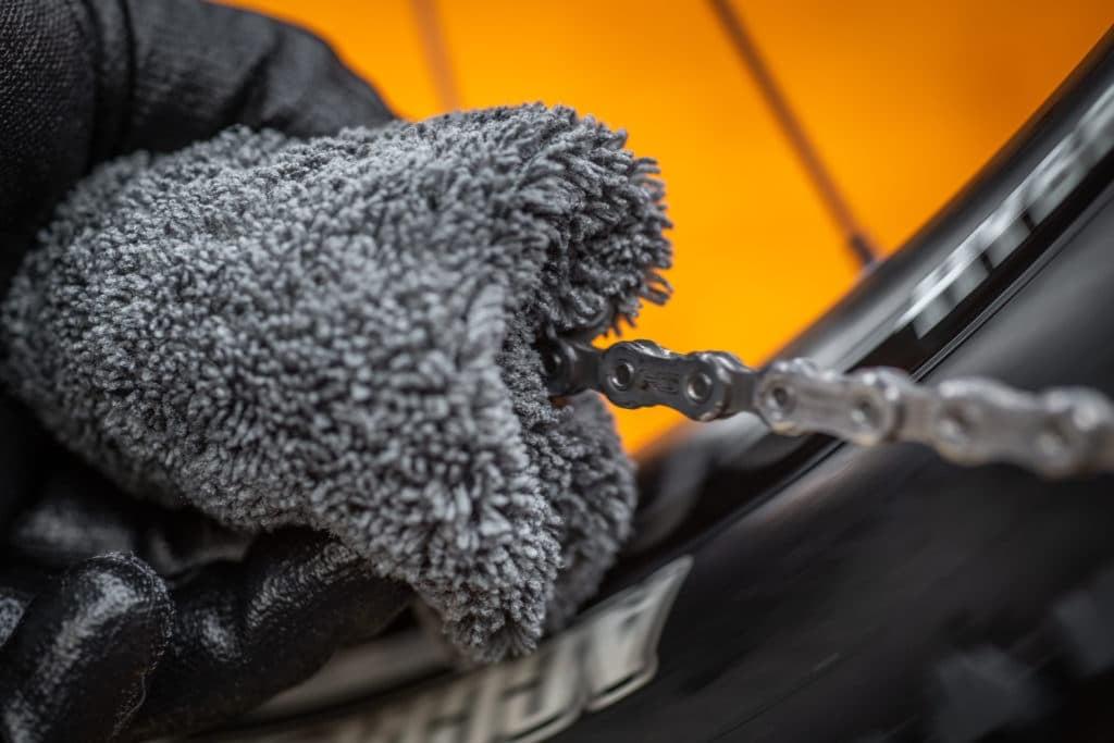 Reinigung einer Fahrradkette mit grauem Tuch und schwarzem Handschuh