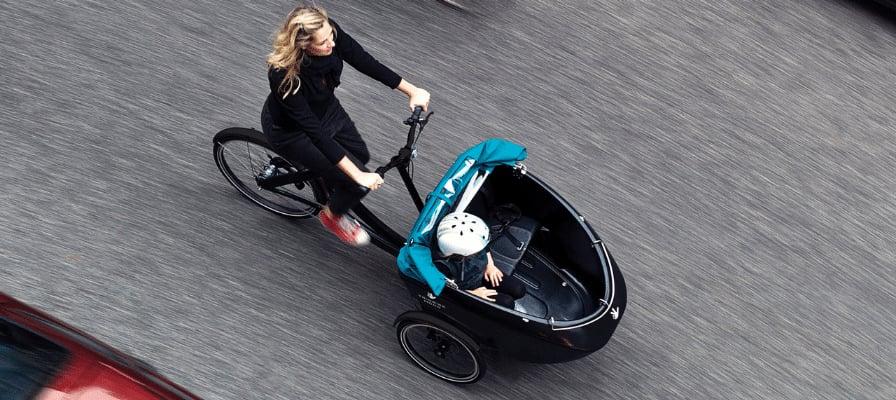 Frau fährt Lastenrad mit Kind durch die Stadt