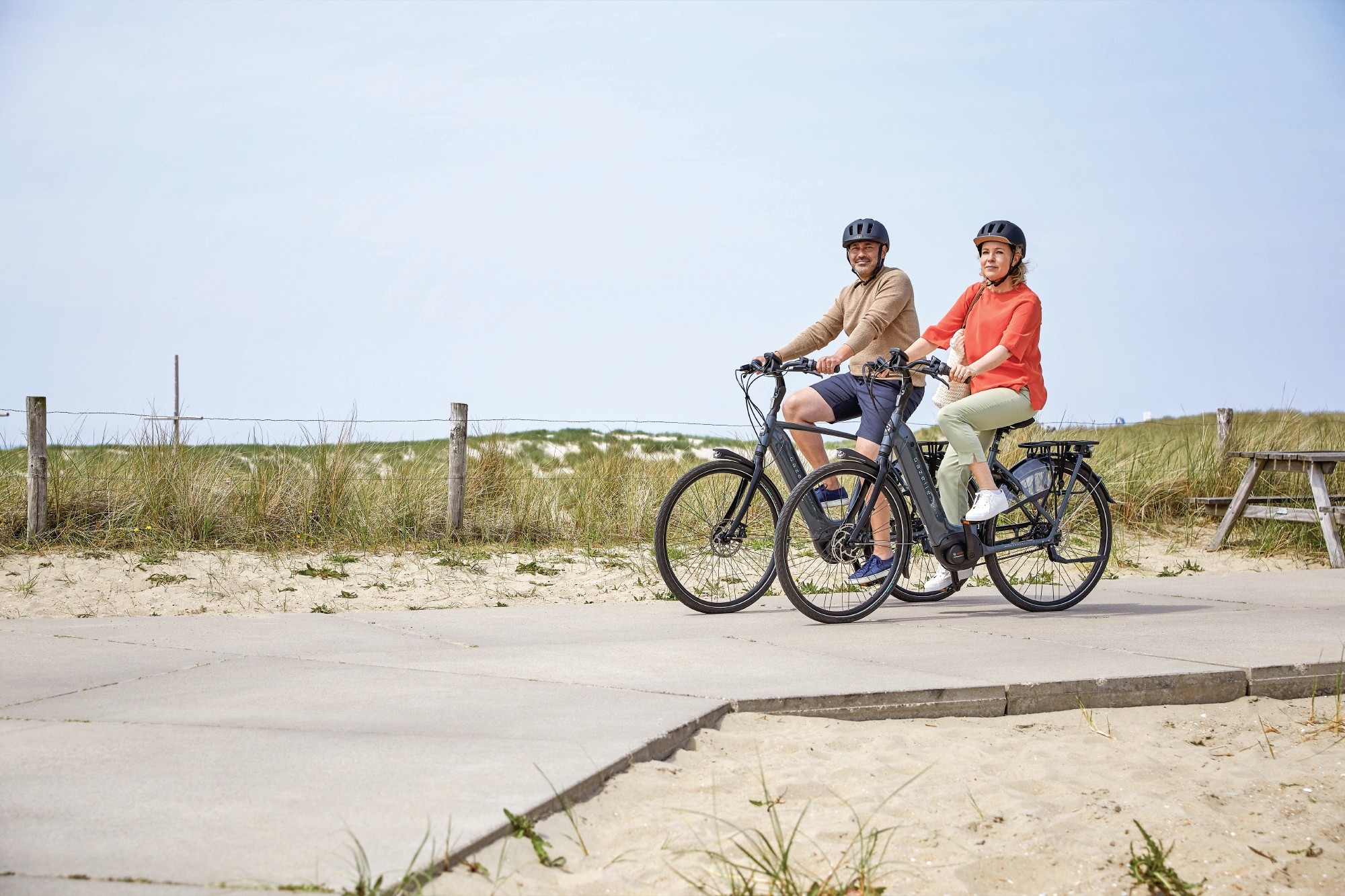 Das Bild zeigt zwei E-Bikes der Marke Gazelle, die in einer malerischen Strandlandschaft positioniert sind.