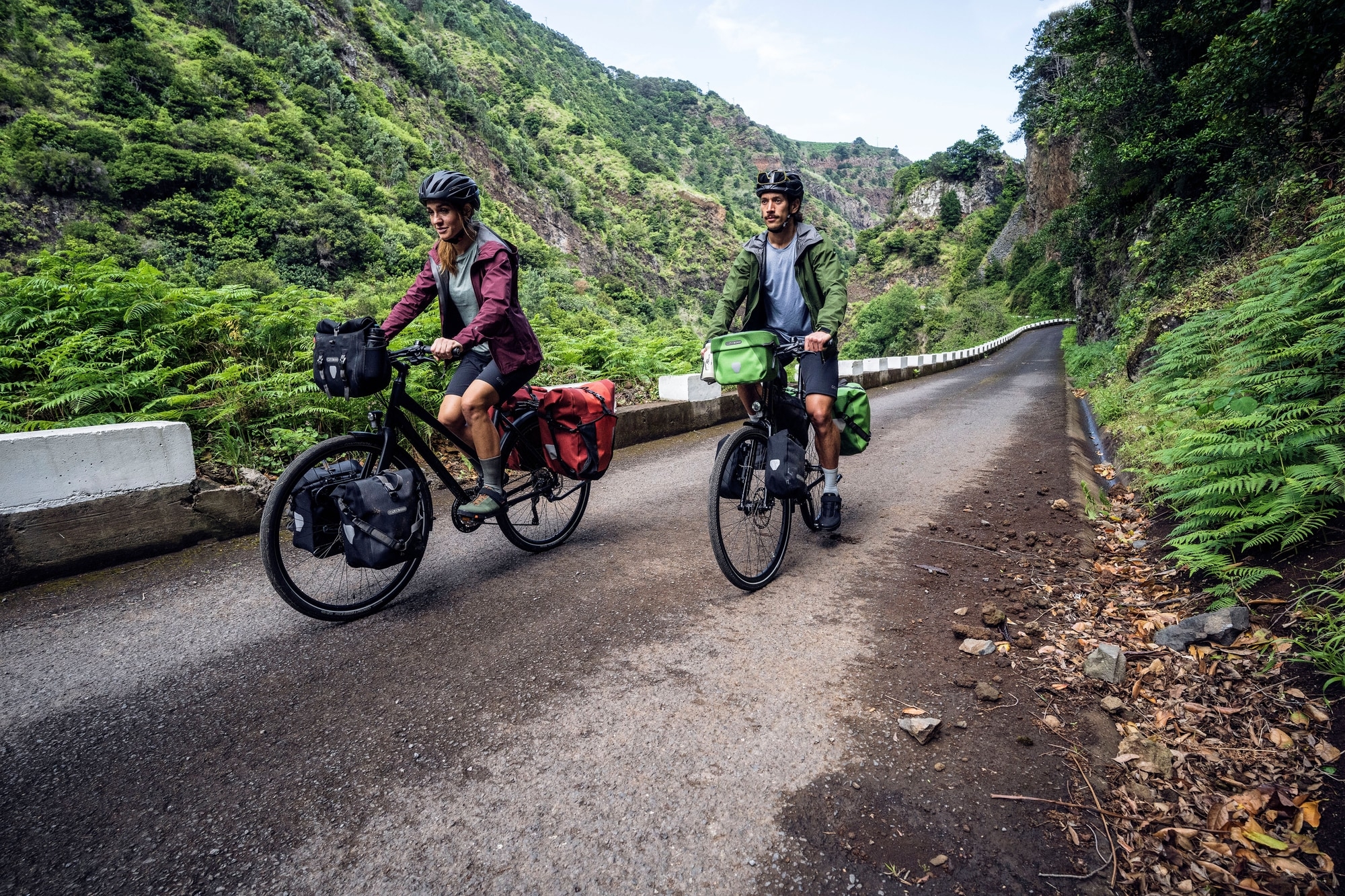 Zwei Radfahrer auf gepackten Fahrrädern erkunden eine beeindruckende, grüne Berglandschaft. Ideales Setup für lange