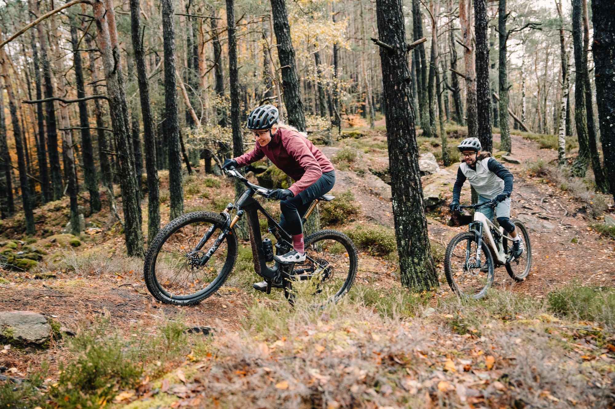 Zwei Personen genießen ein aufregendes Abenteuer auf FOCUS E-Mountainbikes im herbstlichen Wald.
