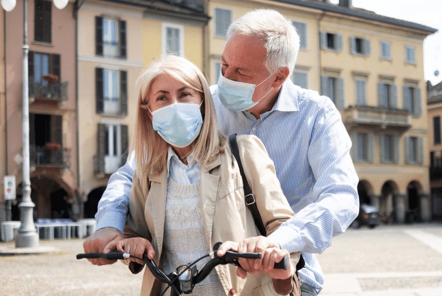 Älteres Paar mit Masken auf Fahrrad in städtischer Umgebung