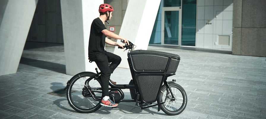 Mann auf Lastenfahrrad vor modernem Gebäude