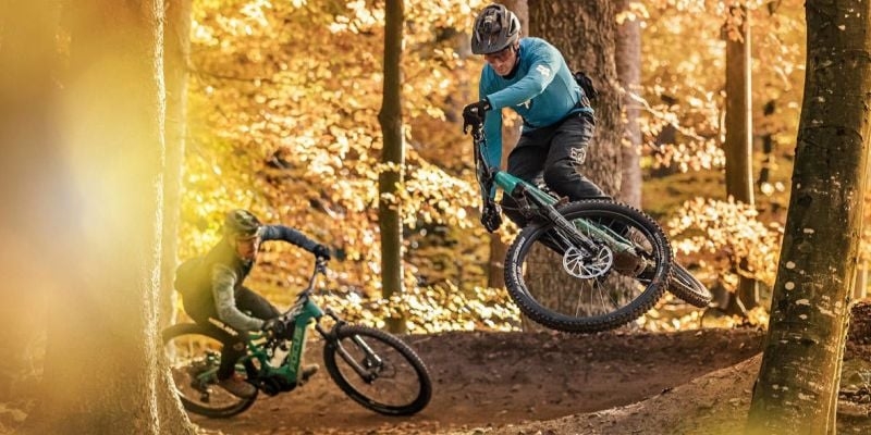 Zwei Mountainbiker im herbstlichen Wald bei Sprung und Abfahrt