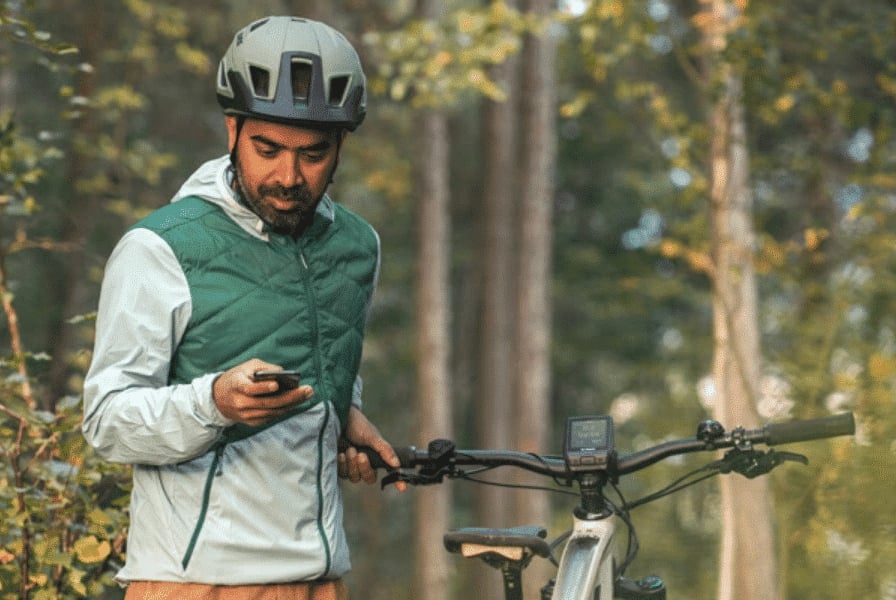 Mann mit Fahrradhelm betrachtet Smartphone im Wald
