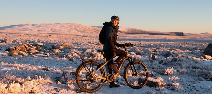 Mann auf E-Bike in verschneiter Landschaft bei Sonnenuntergang